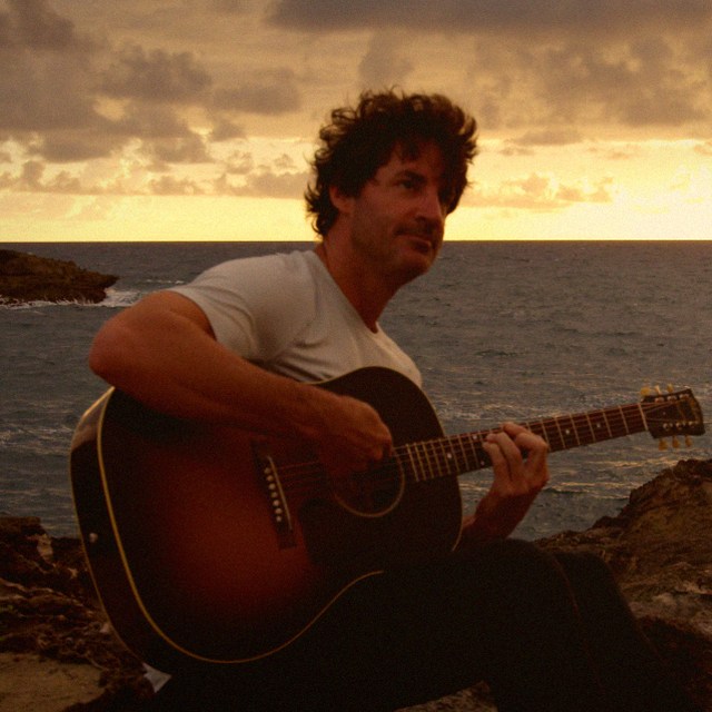 HINZE playing acoustic guitar at sunset by the ocean